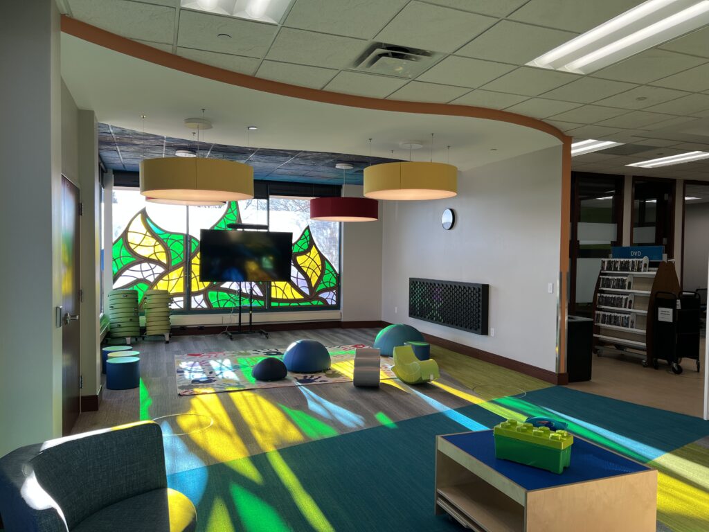 Colorful children’s library activity area with play equipment, creative seating, and bright window artwork