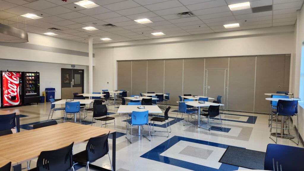 Modern break room with tables, blue chairs, vending machines, and open seating area