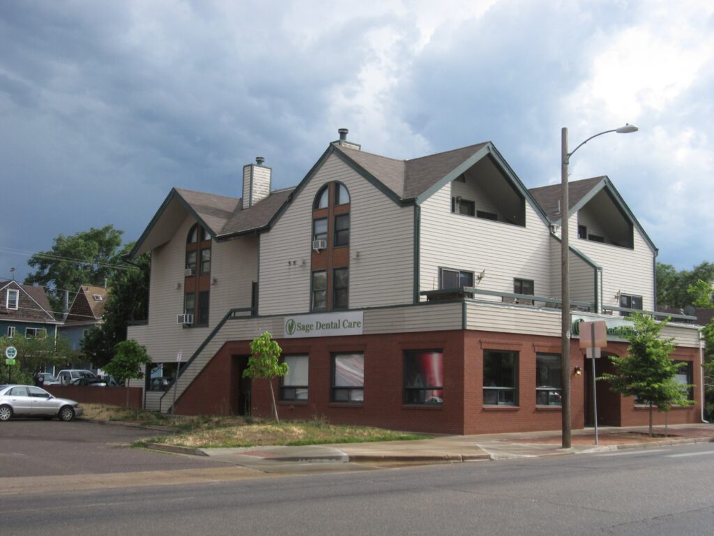 Exterior view of a dental care office building with brick and white siding facade, windows, trees, and street view