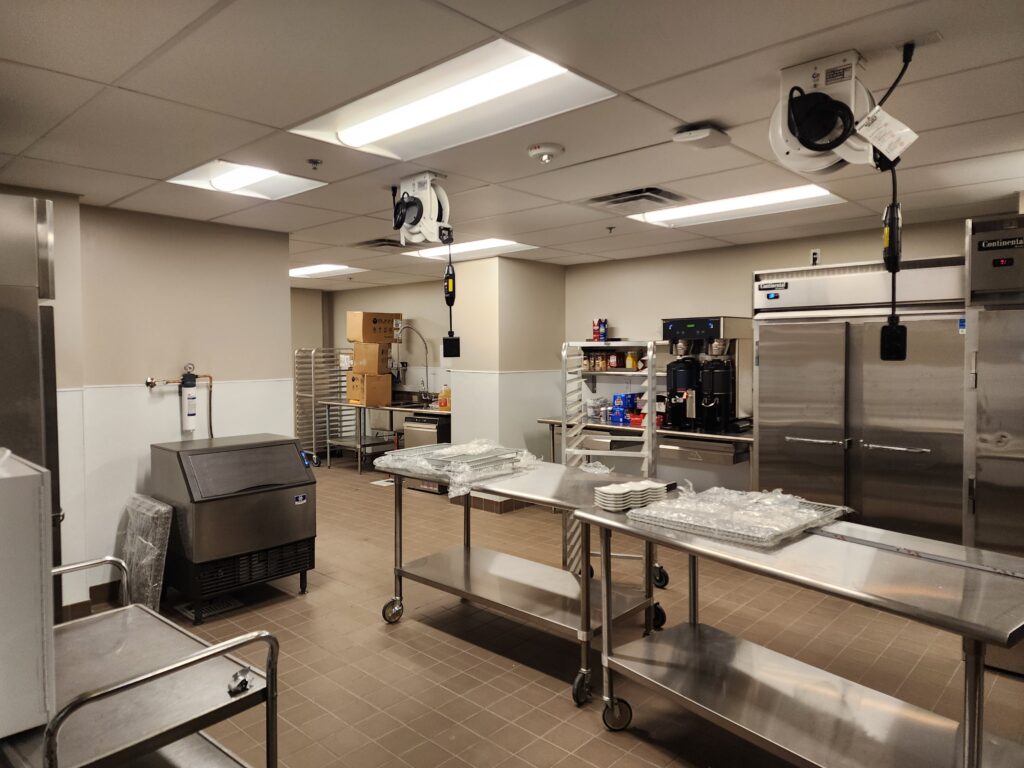 Commercial kitchen with stainless steel equipment, preparation tables, refrigerators, and food service workspace