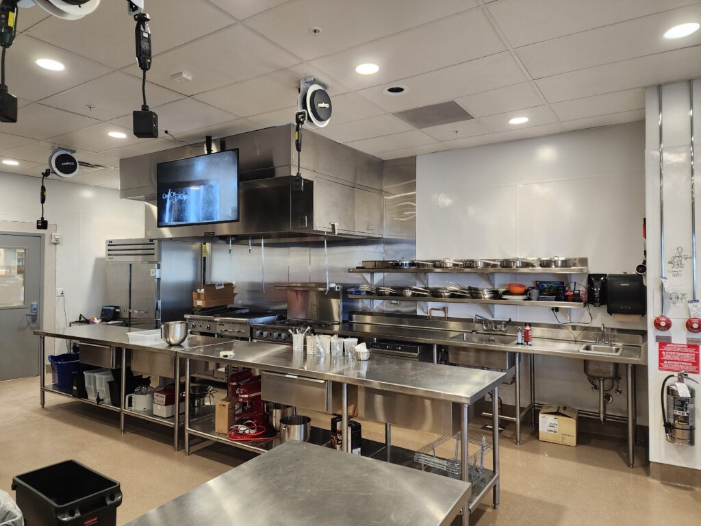 Professional commercial kitchen with stainless steel preparation counters, cooking equipment, and storage shelves