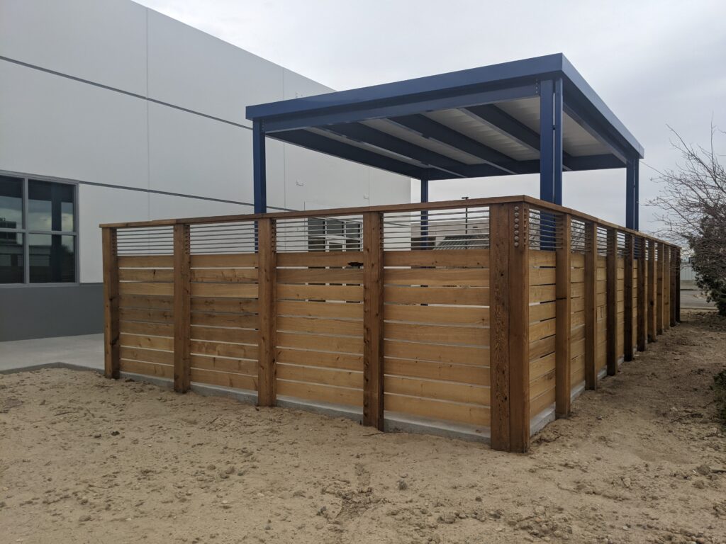 Commercial outdoor patio area with wooden privacy fencing and a modern covered metal canopy structure