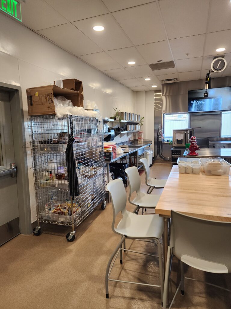 Culinary training kitchen with storage racks, preparation tables, and professional cooking equipment