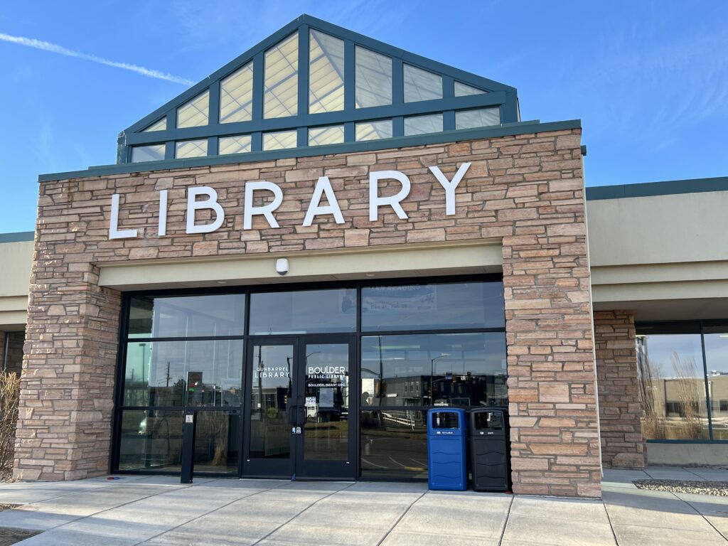 Exterior view of a modern library building entrance with stone walls, glass doors, and large library signage