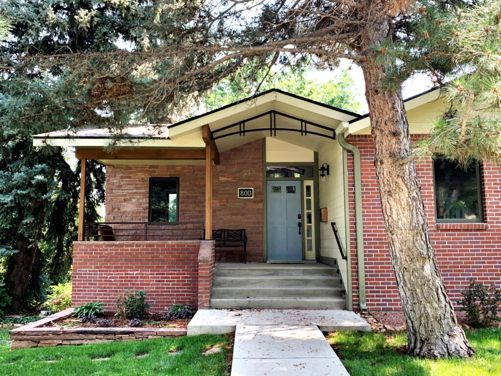 Mid-century modern brick house exterior with front porch, large trees, green lawn, and contemporary entrance design
