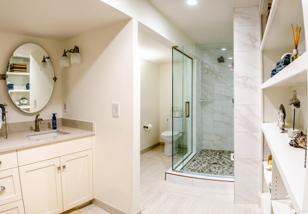 Modern bathroom featuring a glass enclosed shower, white vanity, round mirror, and built-in storage shelves