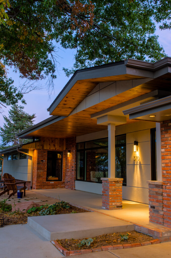 Modern home exterior with brick walls, covered porch, wood ceiling details, large windows, and outdoor lighting
