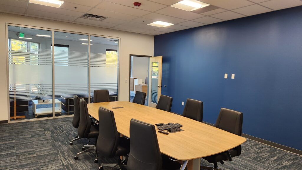Modern office conference room with large meeting table, black chairs, and glass partitions