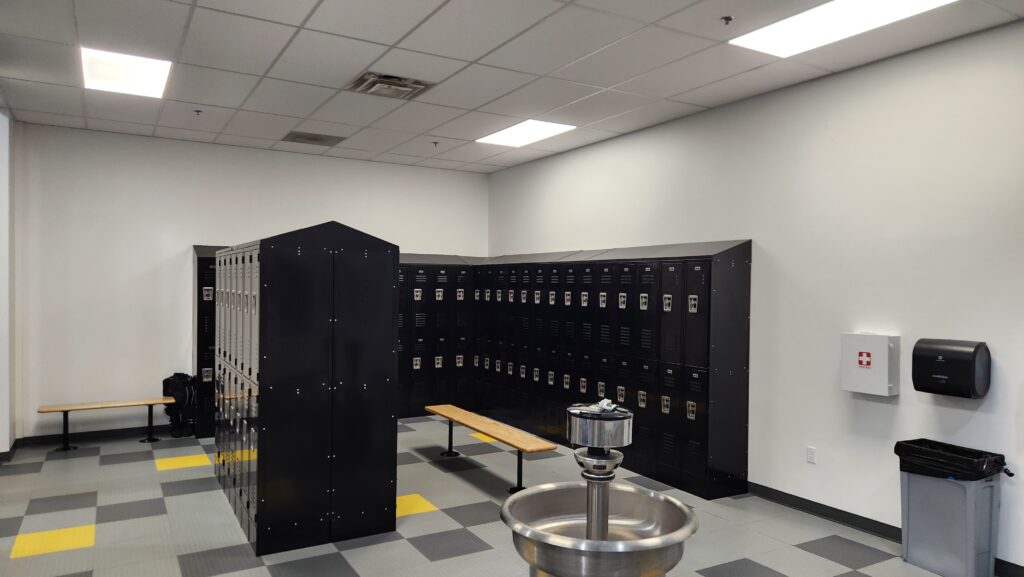 Modern locker room with black storage lockers, benches, drinking fountain, and clean tiled flooring