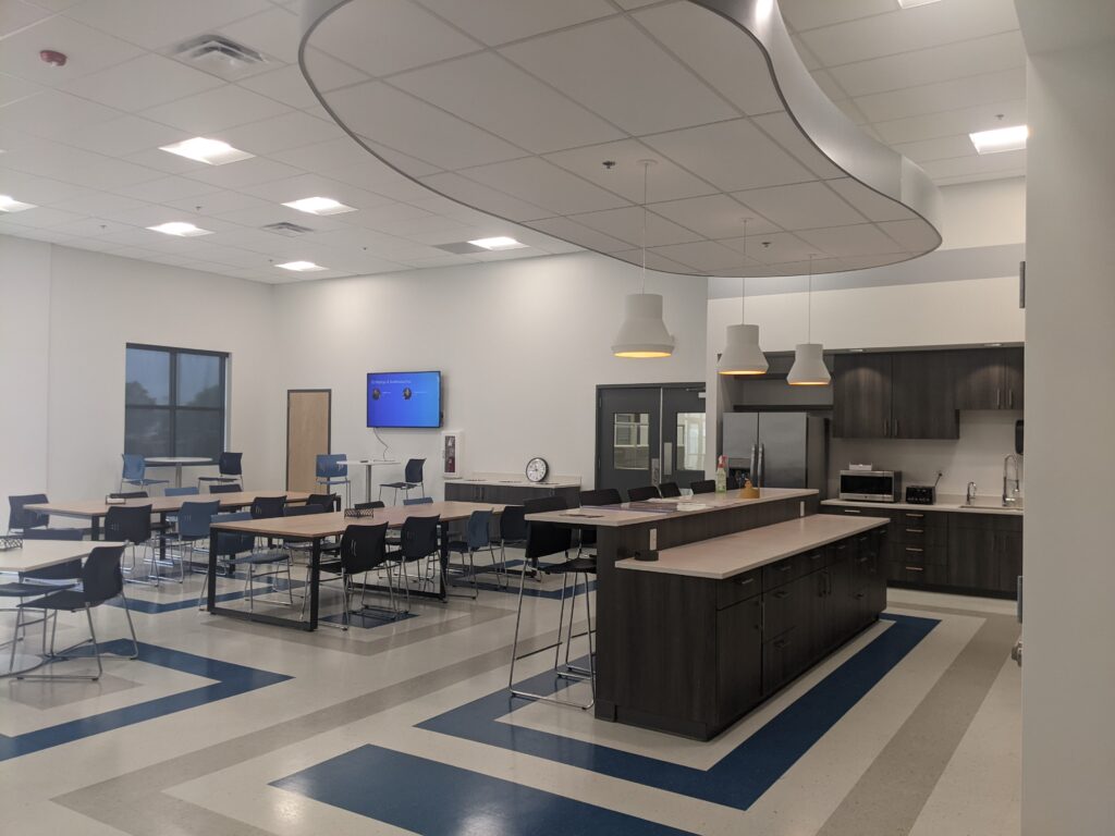 Modern office interior with a collaborative workspace, kitchen area, tables, chairs, and contemporary lighting