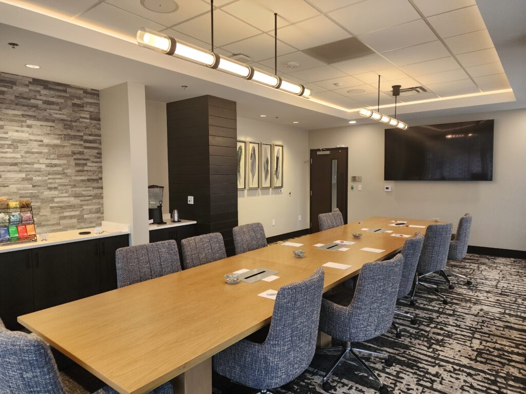 Modern conference room with long wooden table, office chairs, wall-mounted display, and contemporary workspace design