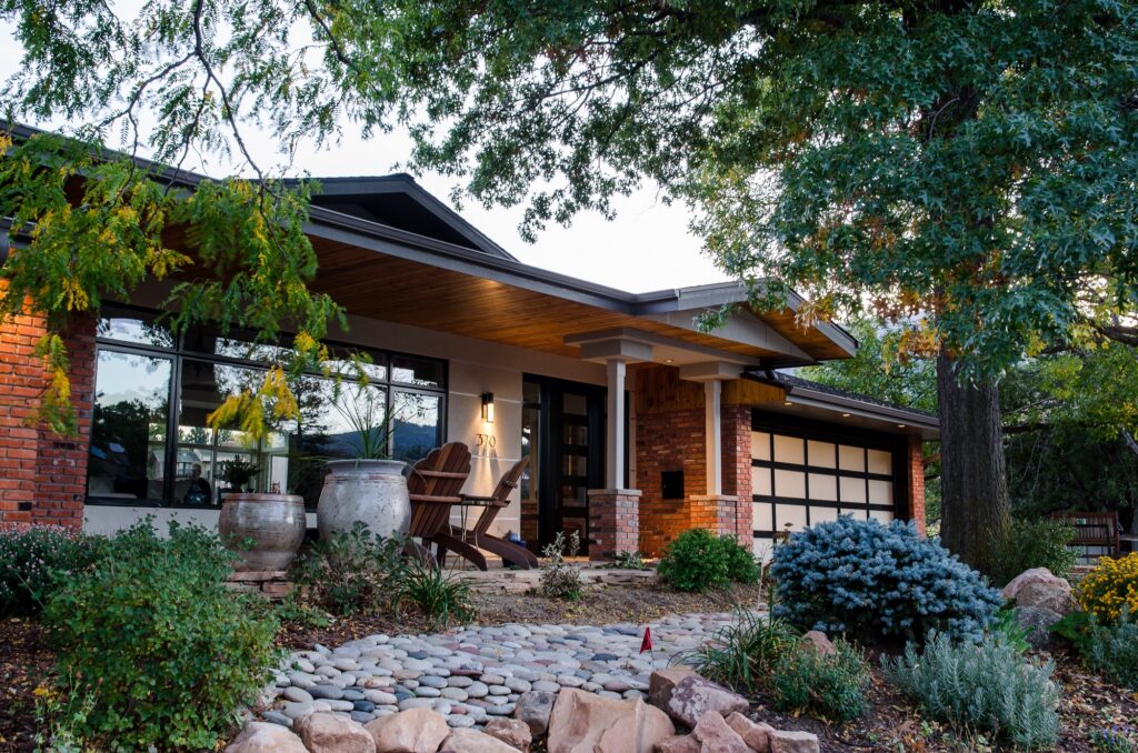 Modern residential home exterior renovation with brick walls, large windows, covered porch, landscaping, and updated outdoor design