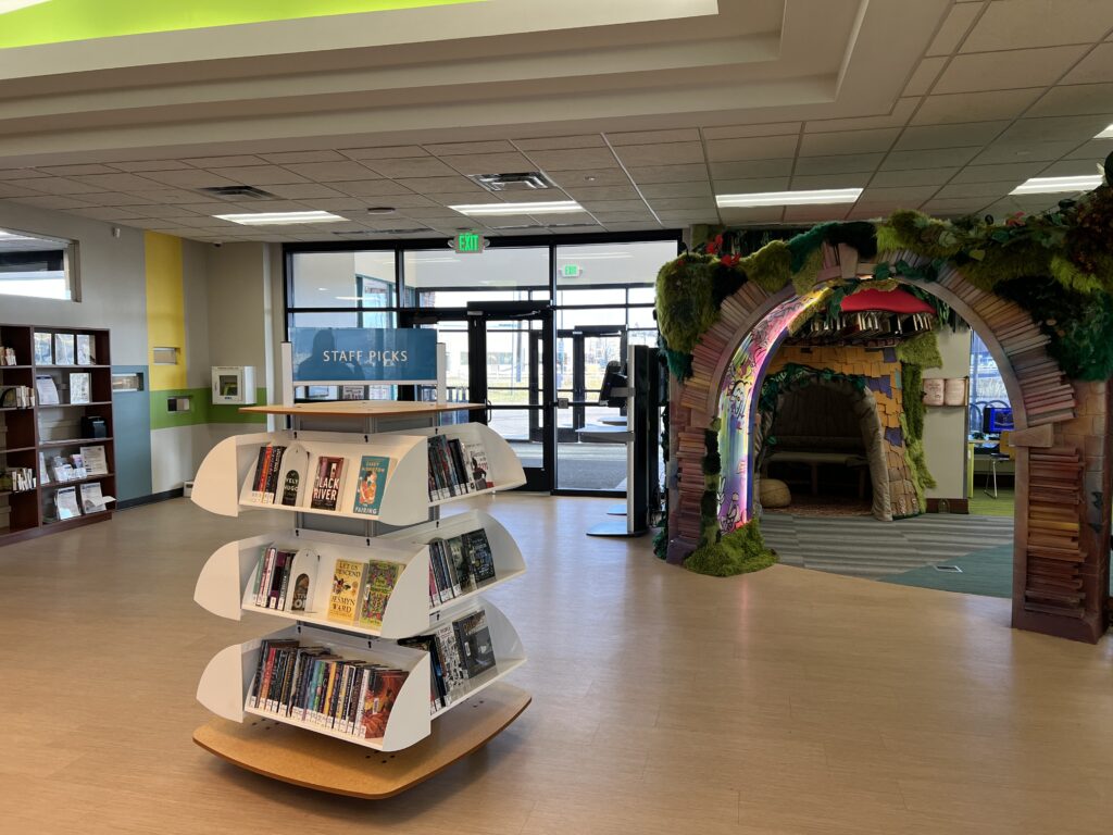 Modern library entrance with staff picks book display, creative reading space, and decorative archway