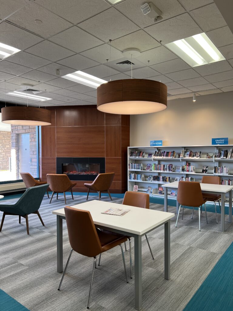 Modern library reading area with bookshelves, study tables, lounge chairs, and contemporary fireplace design