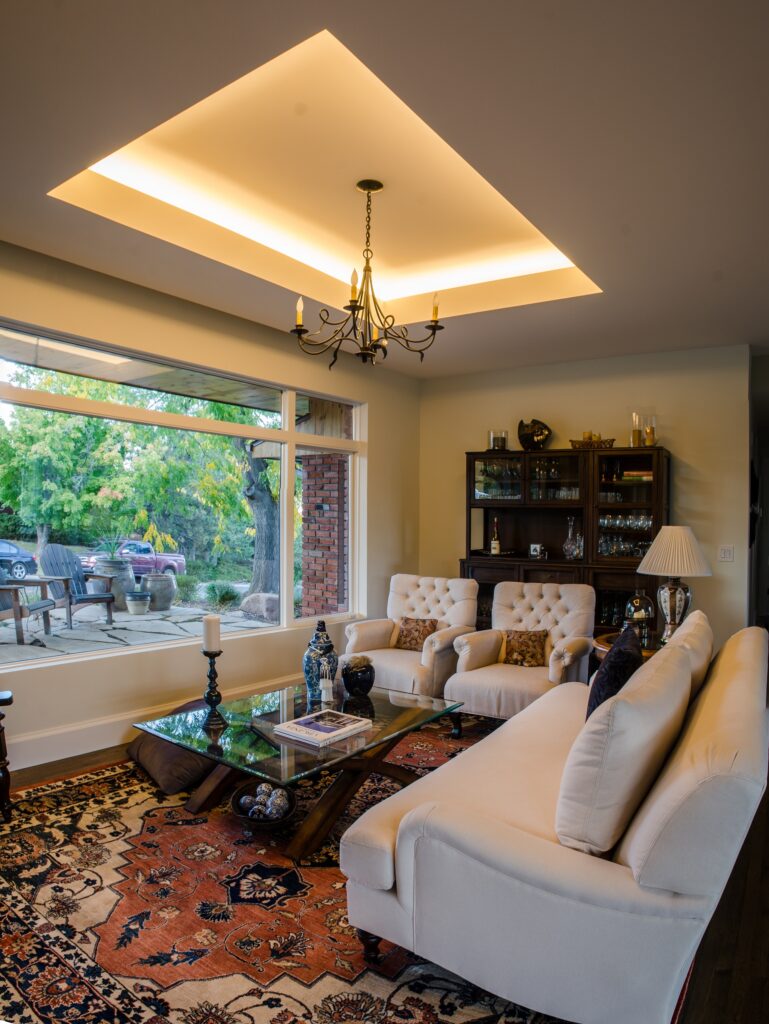 Modern living room with custom tray ceiling, chandelier lighting, elegant furniture, and large windows