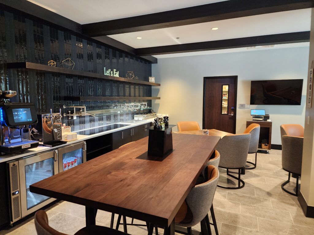 Modern office café lounge with coffee station, wooden tables, seating area, and contemporary interior design