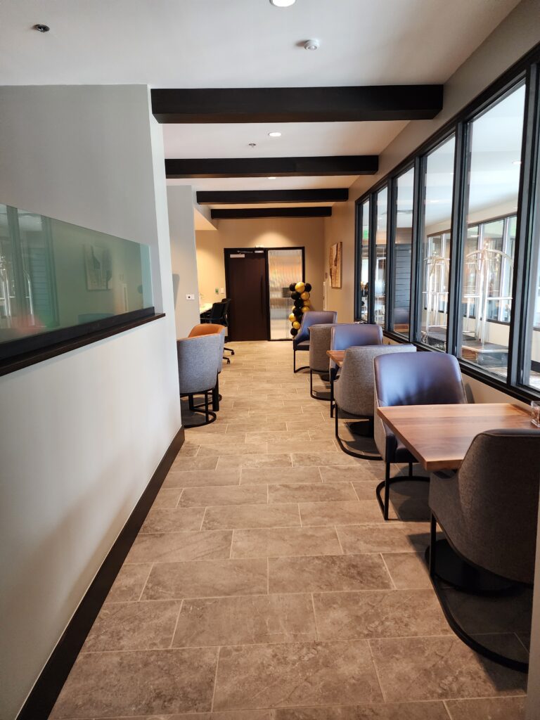 Modern office lounge area with seating, glass windows, wooden tables, and contemporary interior design