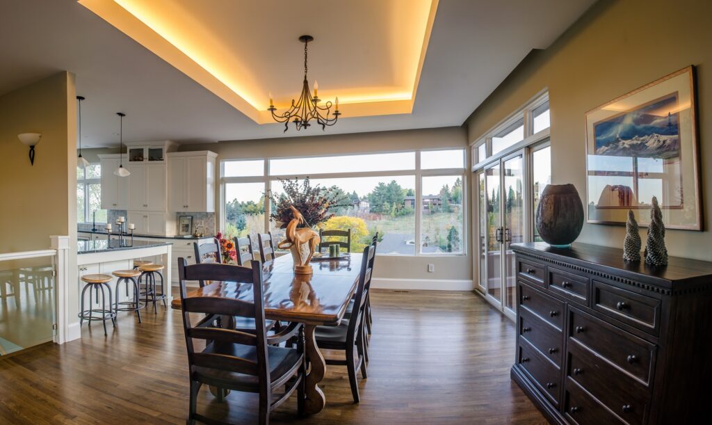 Modern open concept kitchen and dining area with custom cabinets, hardwood flooring, tray ceiling lighting, and large windows