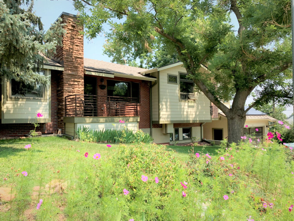 Ranch style home exterior with brick walls, large trees, green lawn, and colorful flower garden