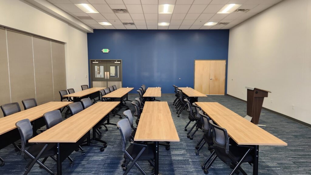 Modern training room with rows of tables, office chairs, presentation podium, and blue accent wall