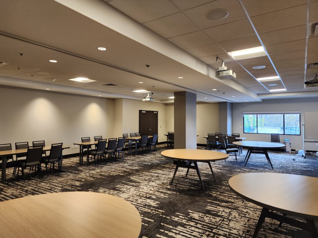 Large modern training room with round tables, office chairs, projector systems, and professional workspace setup