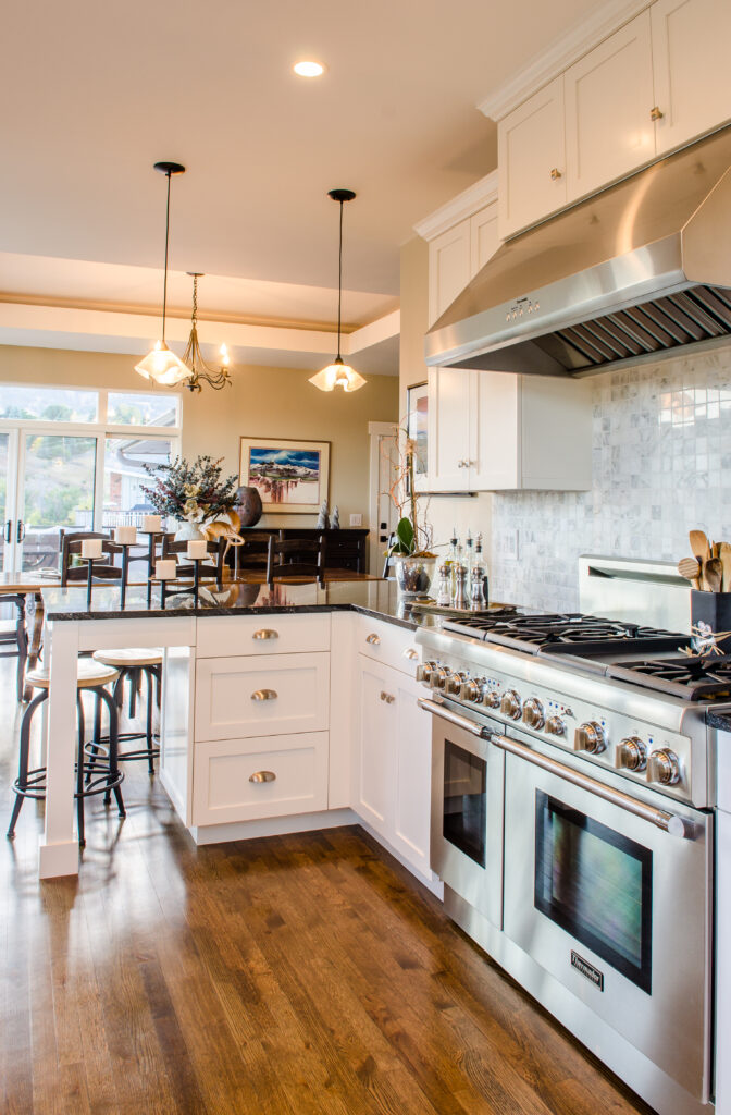 Modern white kitchen featuring stainless steel range, island countertop, pendant lighting, and hardwood flooring