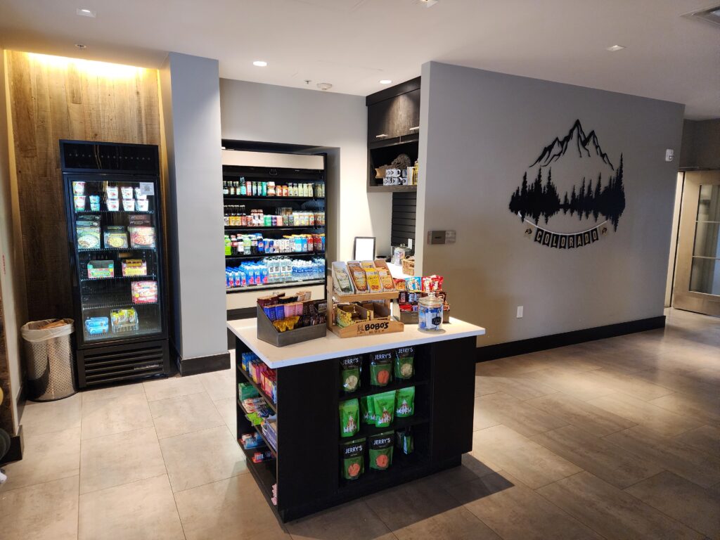 Modern office breakroom with snack shelves, beverage refrigerators, and self-service convenience area