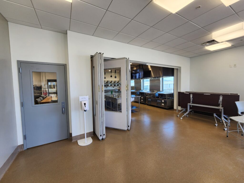 Modern office training room with folding partitions, conference setup, and commercial kitchen area