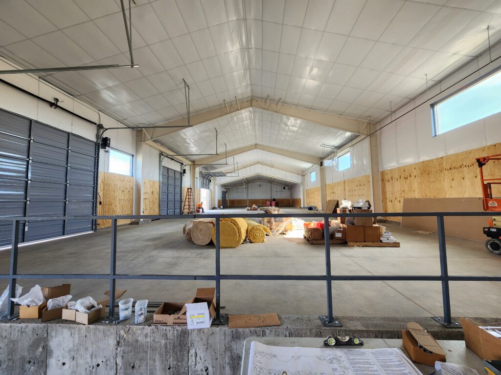 Large agricultural facility interior with high ceilings, open workspace, storage areas, and functional architectural design by PEH Architects