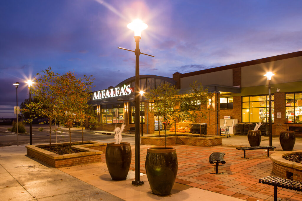 PEH Architects Alafias Plaza evening exterior with illuminated storefronts, brick building, landscaping, and outdoor seating area