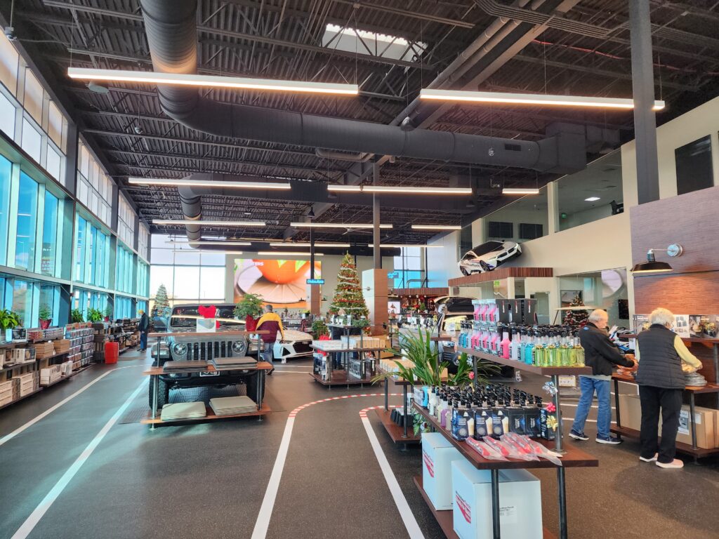 Spacious automotive showroom interior with vehicle displays, retail shelves, modern lighting, and customer areas
