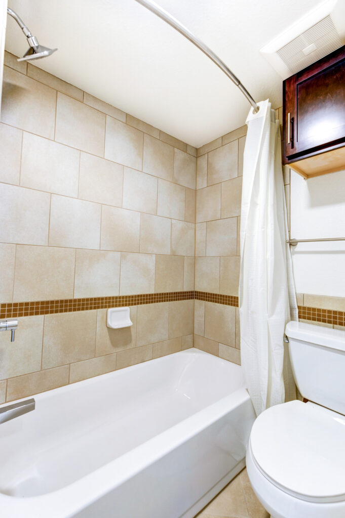 Modern bathroom bathtub and tiled shower interior with contemporary fixtures and storage cabinet
