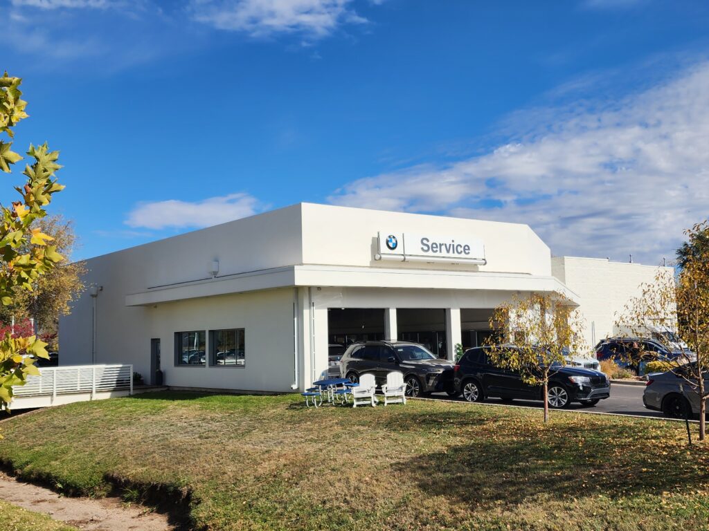 Modern BMW service center building exterior with service entrance, parked vehicles, and landscaped surroundings