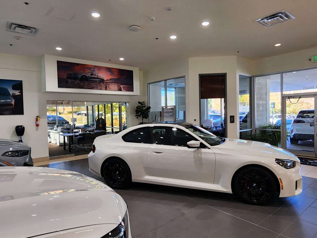 Luxury BMW showroom interior with white vehicle display, glass walls, customer area, and modern automotive retail design