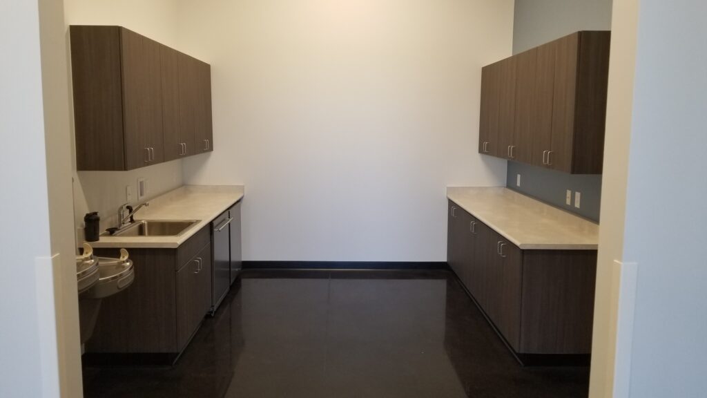 Modern commercial breakroom interior with built-in cabinets, countertops, sink area, and functional workplace design by PEH Architects
