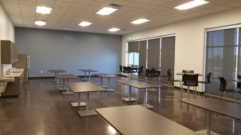 Modern commercial breakroom with tables, seating areas, kitchenette, and flexible workplace interior design by PEH Architects
