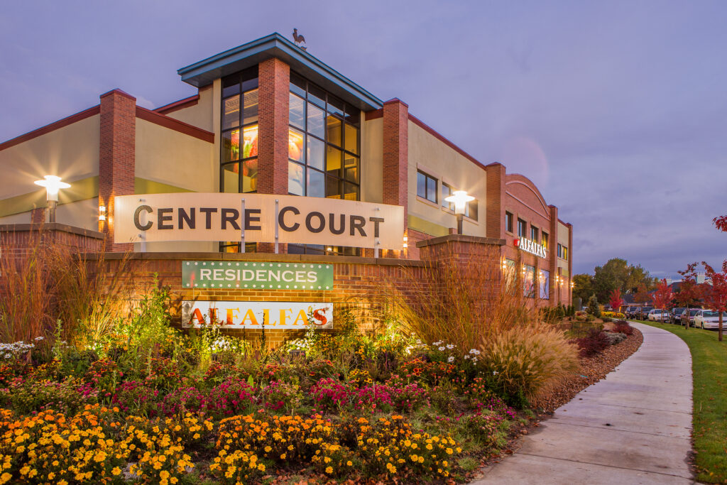Commercial campus building exterior with brick facade, glass entrance, landscaped garden, signage, and modern architectural design