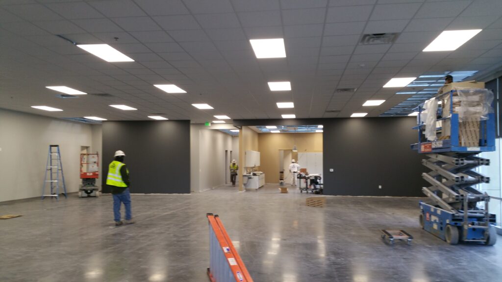 Commercial building interior during construction with workers, polished flooring, lighting installation, and unfinished workspace area