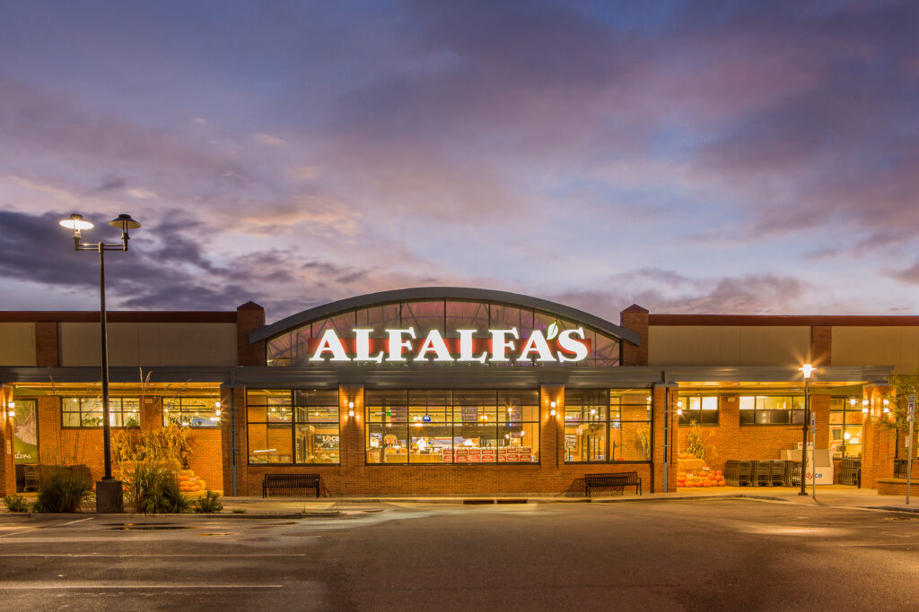Modern retail building exterior at dusk with illuminated storefront, curved entrance facade, brick walls, and architectural lighting