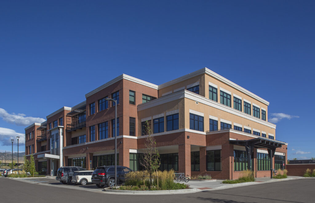Contemporary office building exterior with brick facade, glass windows, parking area, and modern architectural design
