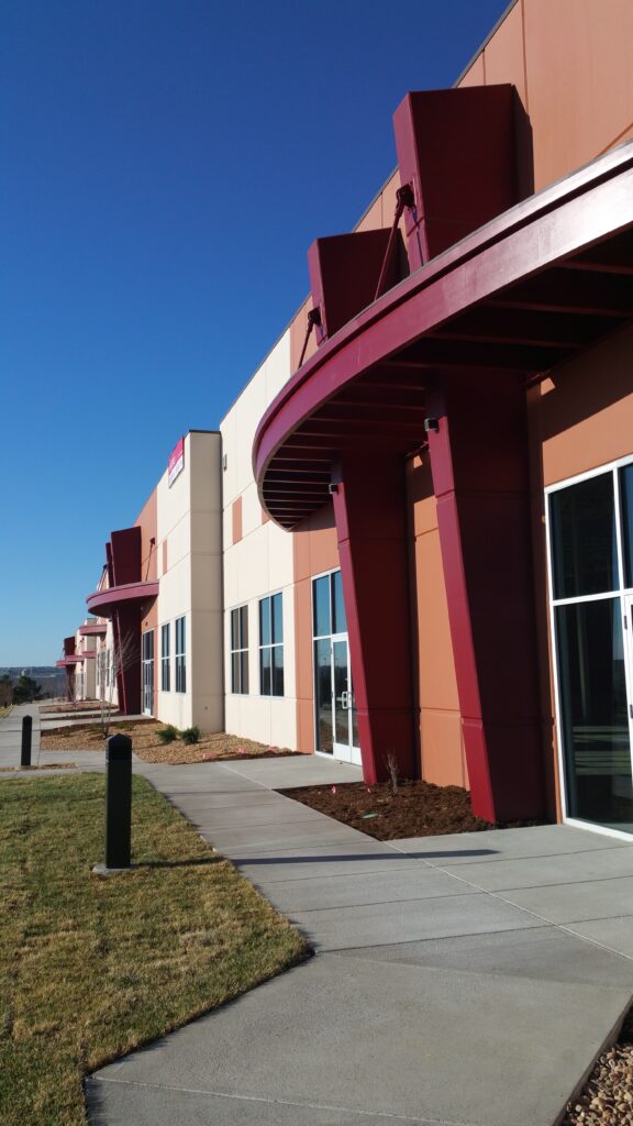 Modern industrial building exterior with curved entrance canopy, glass doors, and landscaped walkway