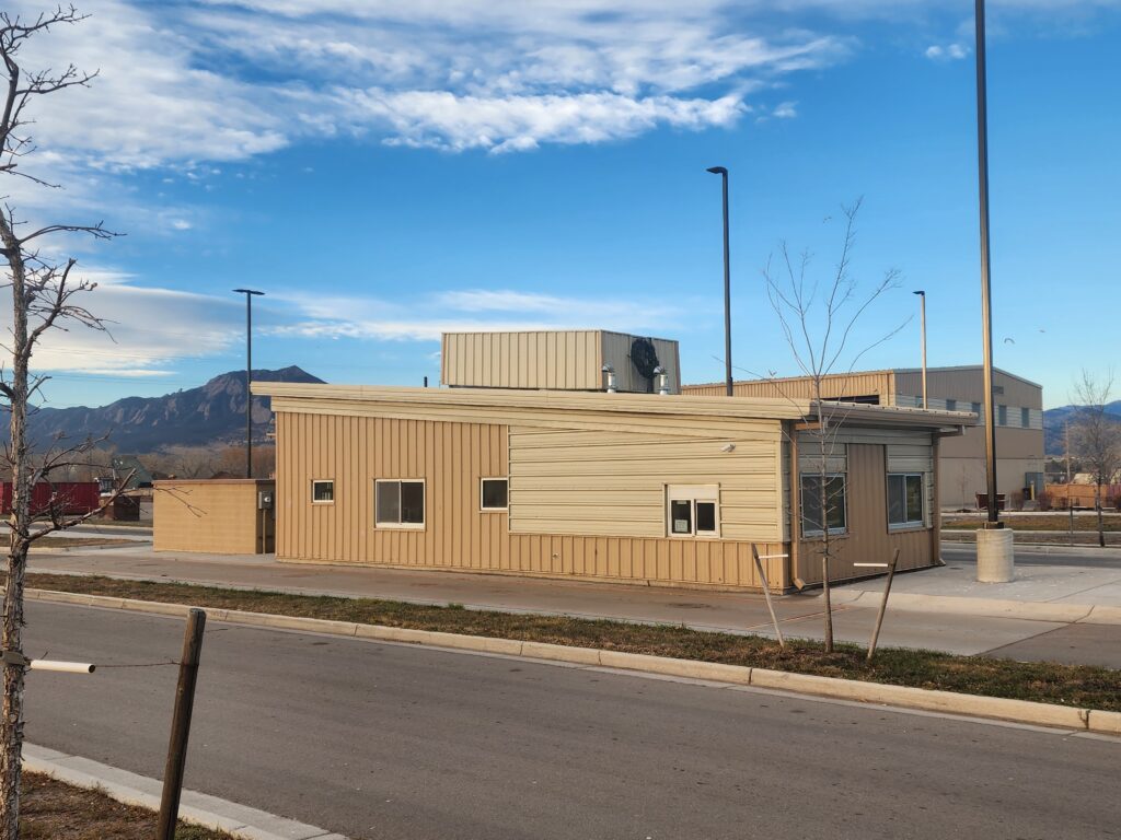 Exterior view of an industrial facility building with metal siding, service areas, and mountain landscape background