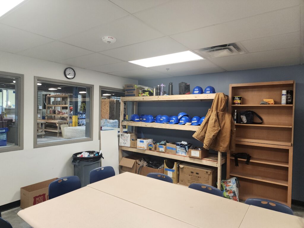 Industrial facility safety training room with meeting table, storage shelves, protective helmets, and workplace equipment