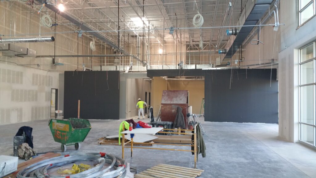 Large industrial interior space during construction with exposed HVAC systems, electrical wiring, and partition walls