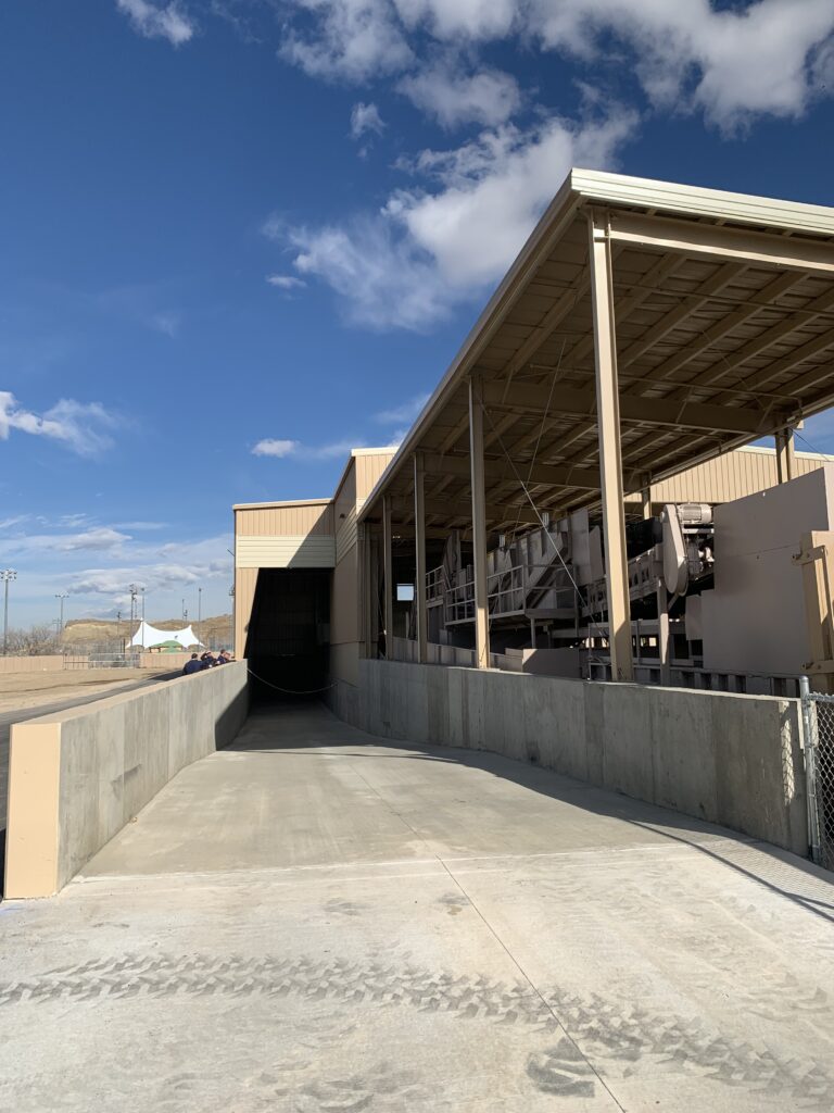 Industrial processing facility exterior with covered loading area, concrete ramp, and large-scale equipment structure