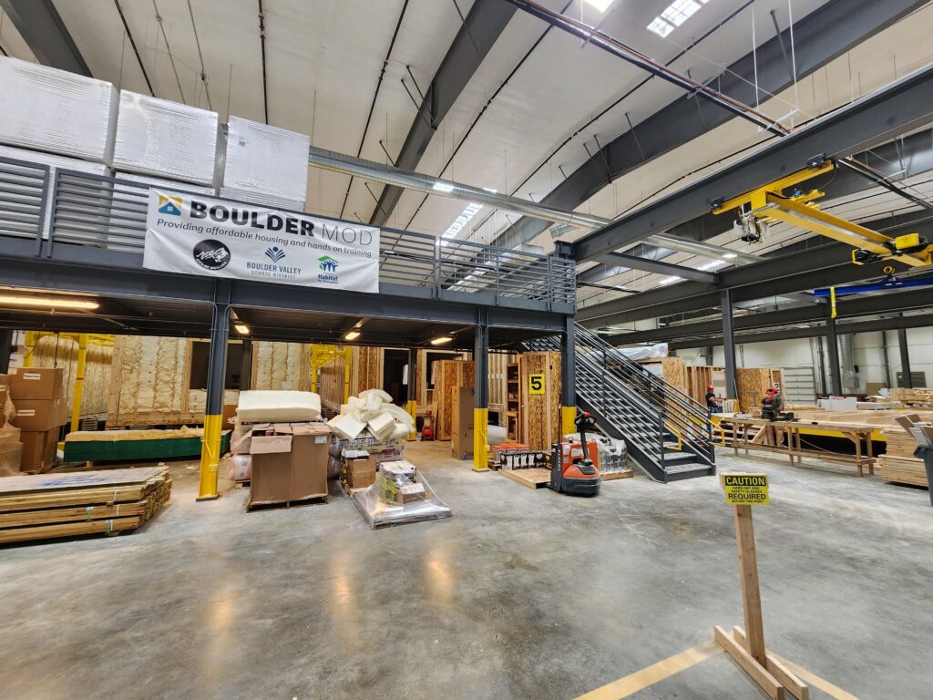 Large industrial workshop interior with elevated platform, safety equipment, construction materials, and manufacturing workspace