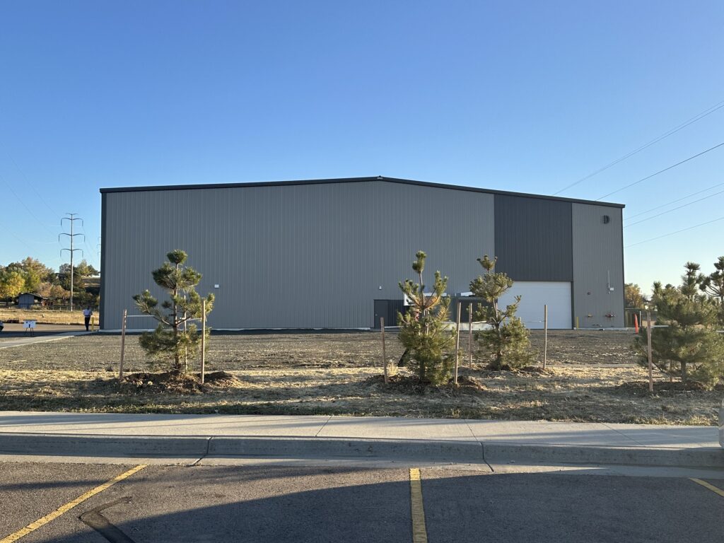 Modern industrial warehouse building exterior with metal siding, loading area, and landscaped surroundings
