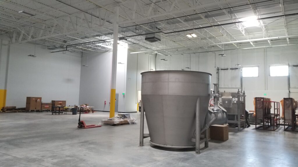 Large industrial warehouse interior featuring processing equipment, concrete flooring, exposed ceiling systems, and open manufacturing space