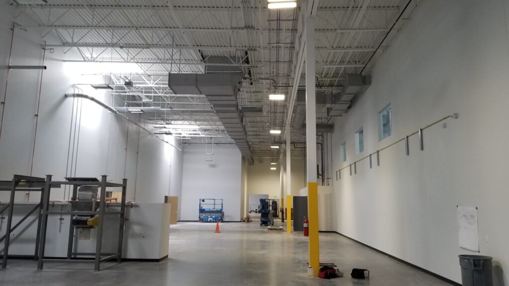 Large industrial warehouse interior with high ceilings, exposed mechanical systems, open workspace, and functional facility design by PEH Architects
