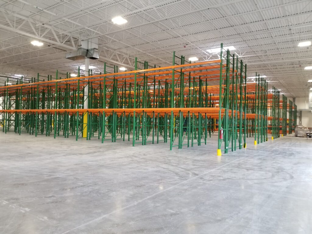 Large industrial warehouse interior with green and orange storage racks, concrete flooring, and high ceiling design